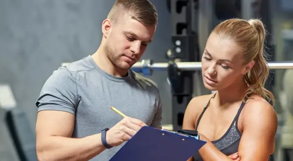 Un personal trainer que es, explica un plan de entrenamiento a una mujer en un gimnasio.