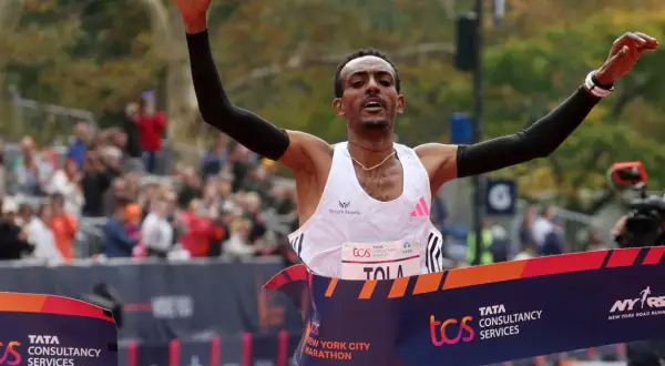 Tamirat Tola cruza la meta de la Maratón de Nueva York, victorioso, con los brazos en alto.