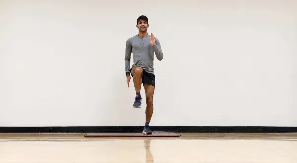 Hombre realizando ejercicio de pliometría para corredores, levantando una rodilla y extendiendo un brazo.