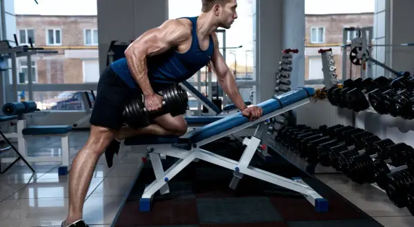 Hombre musculoso haciendo remo inclinado con mancuerna en un gimnasio.