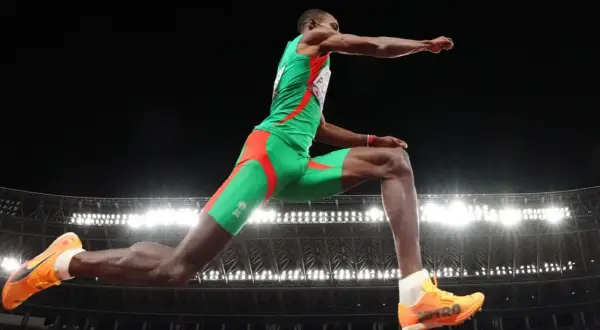Pedro Pablo Pichardo en pleno salto triple, demostrando su potencia y técnica en el aire, con el estadio iluminado de fondo.