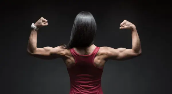 Mujer con espalda musculosa y brazos flexionados, mostrando su fuerza. El óxido nítrico para qué sirve: potencia el rendimiento deportivo.