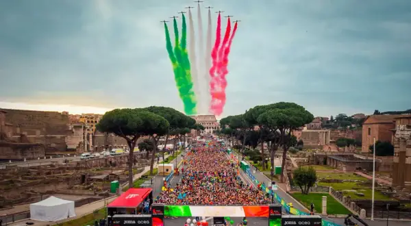 La **media maratón Roma** comienza con aviones dibujando la bandera italiana en el cielo, sobre una multitud de corredores y el Coliseo al fondo.