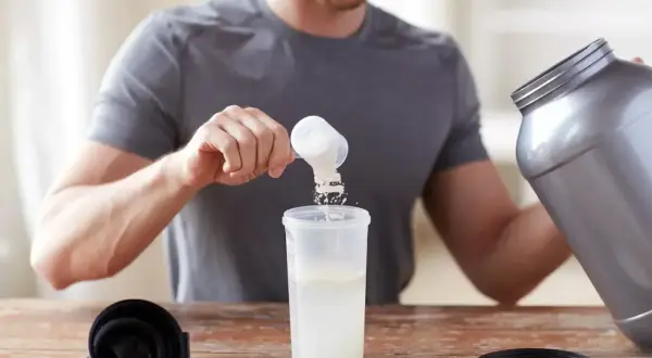 Hombre preparando su batido de proteina con agua o leche. Añade el polvo a un vaso mezclador.