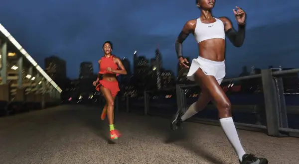 Dos corredoras entrenan al anochecer en la ciudad, aprendiendo como respirar al correr para mejorar su rendimiento.