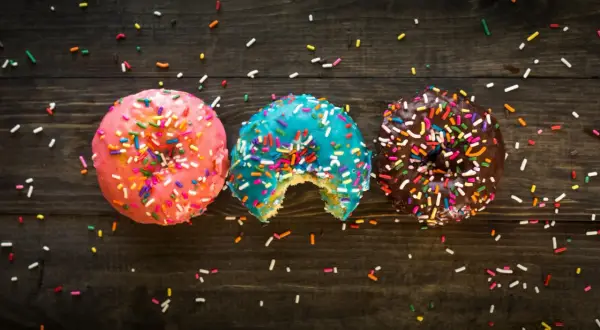 Tres donas coloridas con chispas, una mordida en la azul. ¡Un festín visual que desafía la dieta inversa!