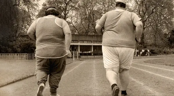 Dos personas con sobrepeso corren en una pista, un paso a la vez para adelgazar.