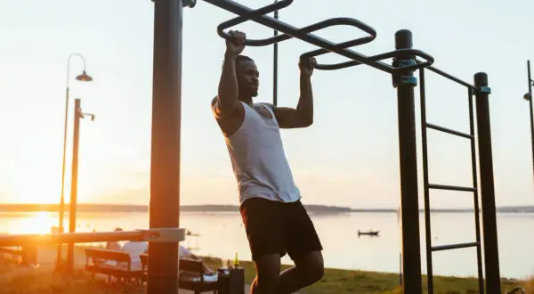 Hombre entrenando en barra exterior, aprendiendo como hacer dominadas al atardecer.