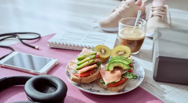 Dos sándwiches con aguacate y jamón serrano, ideales para que picar entre horas saludable. Junto a unas zapatillas deportivas y café.