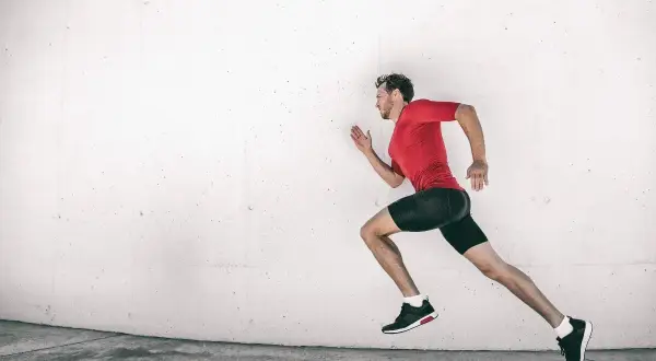 Corredor en pleno entrenamiento maratón, con ropa deportiva roja y negra, contra una pared de hormigón.