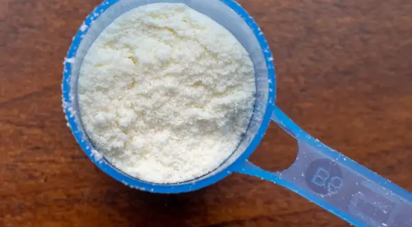 Cuchara dosificadora azul llena de polvo blanco, quizás proteína en polvo. ¿Tomar proteínas es malo?
