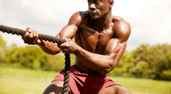 Hombre musculoso en entrenamiento espartano, tirando de una cuerda con fuerza.