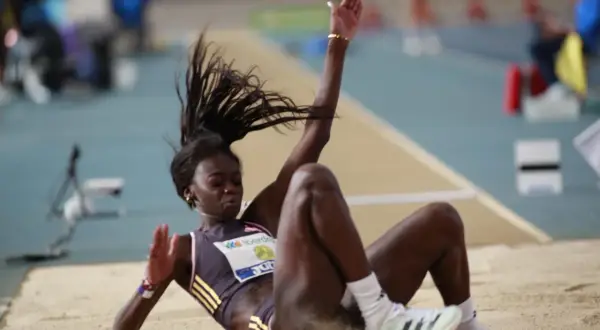Atleta en pleno salto de longitud femenino, aterrizando en la arena con el cabello al viento.