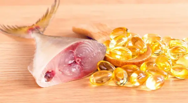 Un trozo de pescado fresco junto a cápsulas doradas, representando los **aceite de hígado de bacalao beneficios** para la salud.