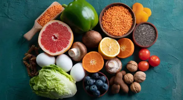 Variedad de alimentos alcalinos lista: lentejas, pomelo, pimiento verde, champiñones, limón, naranjas, tomates, arándanos, huevos, lechuga, pasta integral, semillas de chía, nueces y tamarindos.