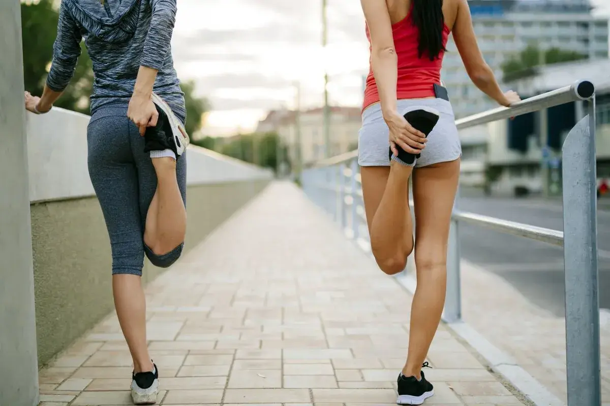 Dos mujeres estiran sus piernas en un puente. Saben que es bueno correr todos los días para mantenerse en forma.