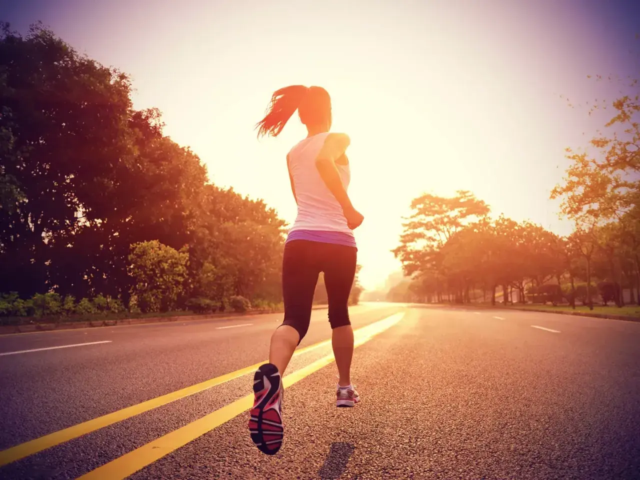 Mujer corriendo por una carretera al atardecer, entrenando para la distancia media maratón.