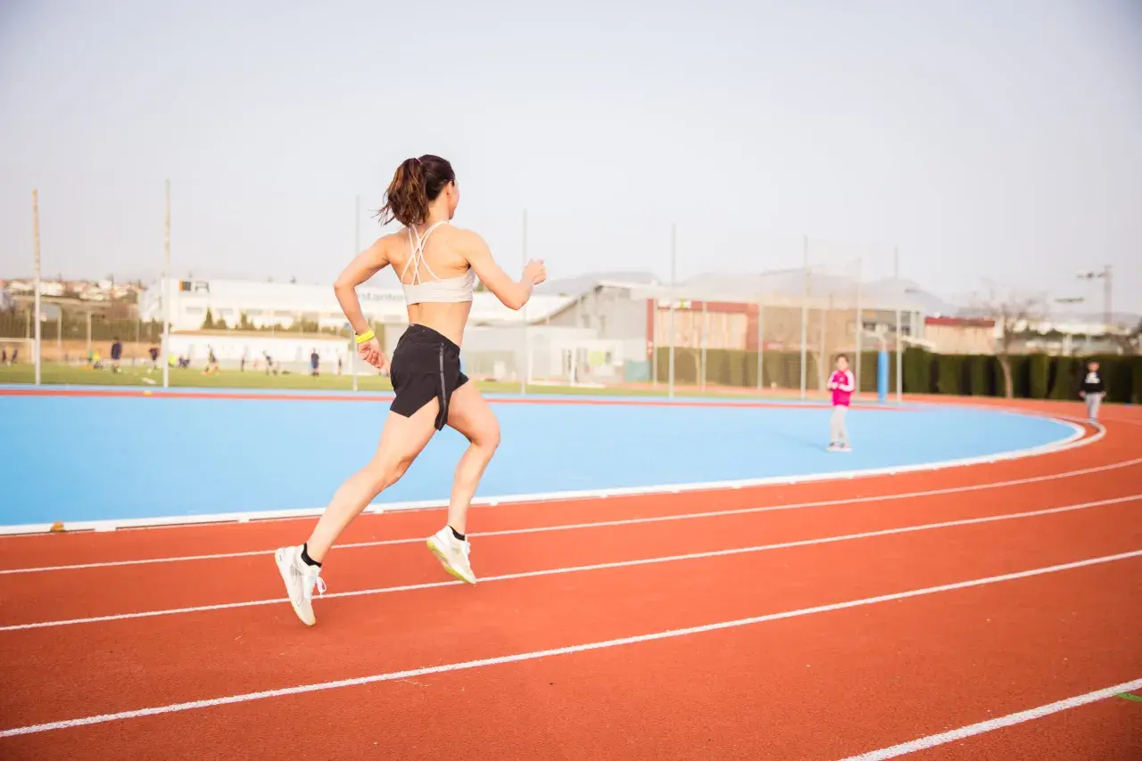 Mujer corriendo en pista de atletismo, lista para las noticias running.