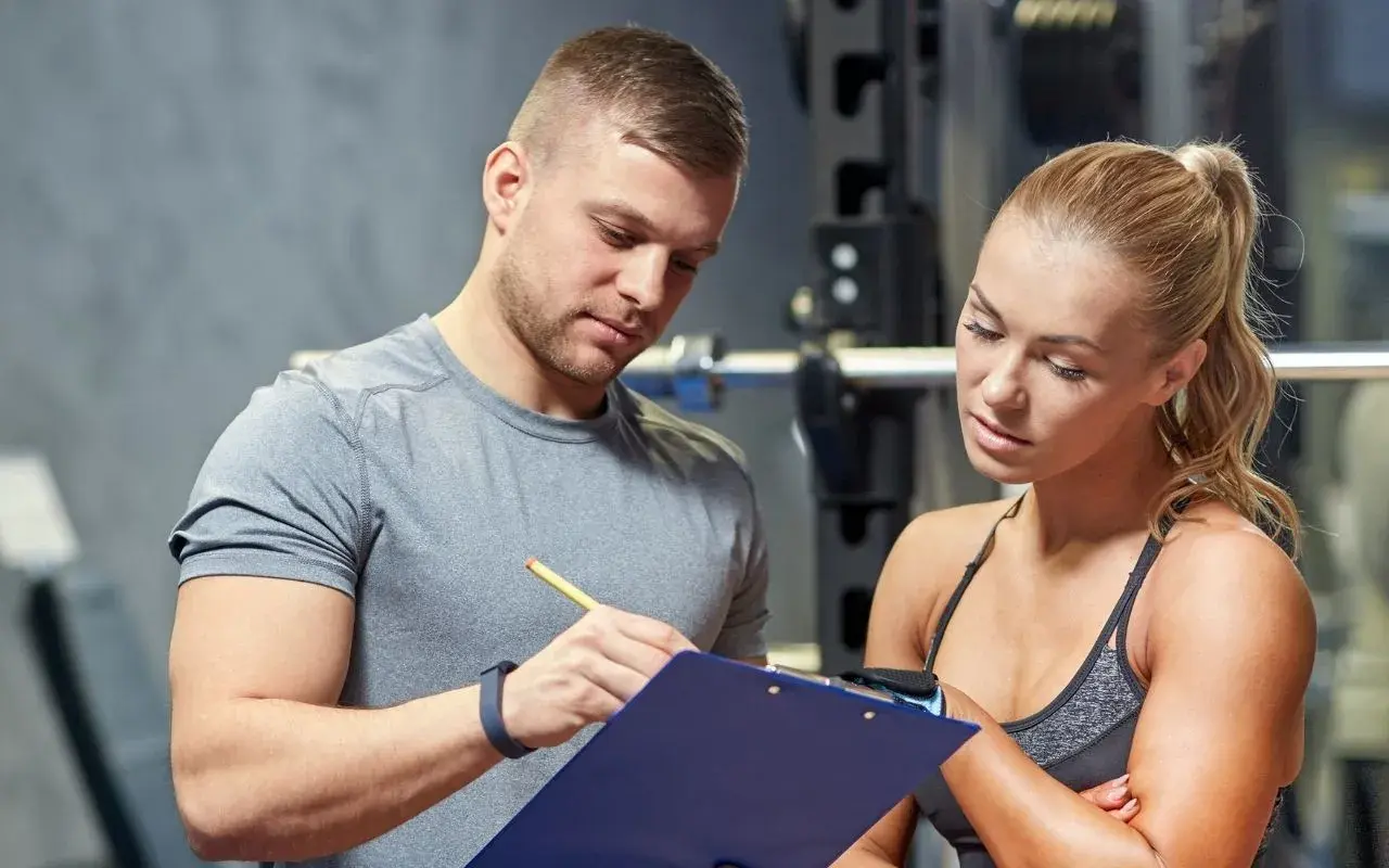 Un personal trainer que es, explica un plan de entrenamiento a una mujer en un gimnasio.