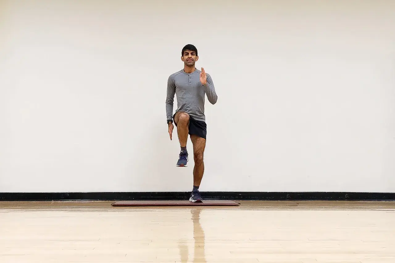 Hombre realizando ejercicio de pliometría para corredores, levantando una rodilla y extendiendo un brazo.