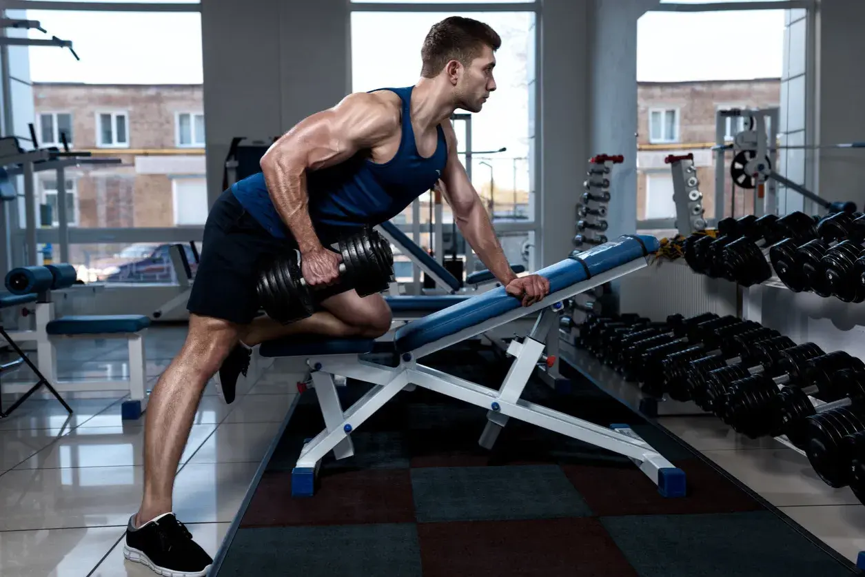 Hombre musculoso haciendo remo inclinado con mancuerna en un gimnasio.