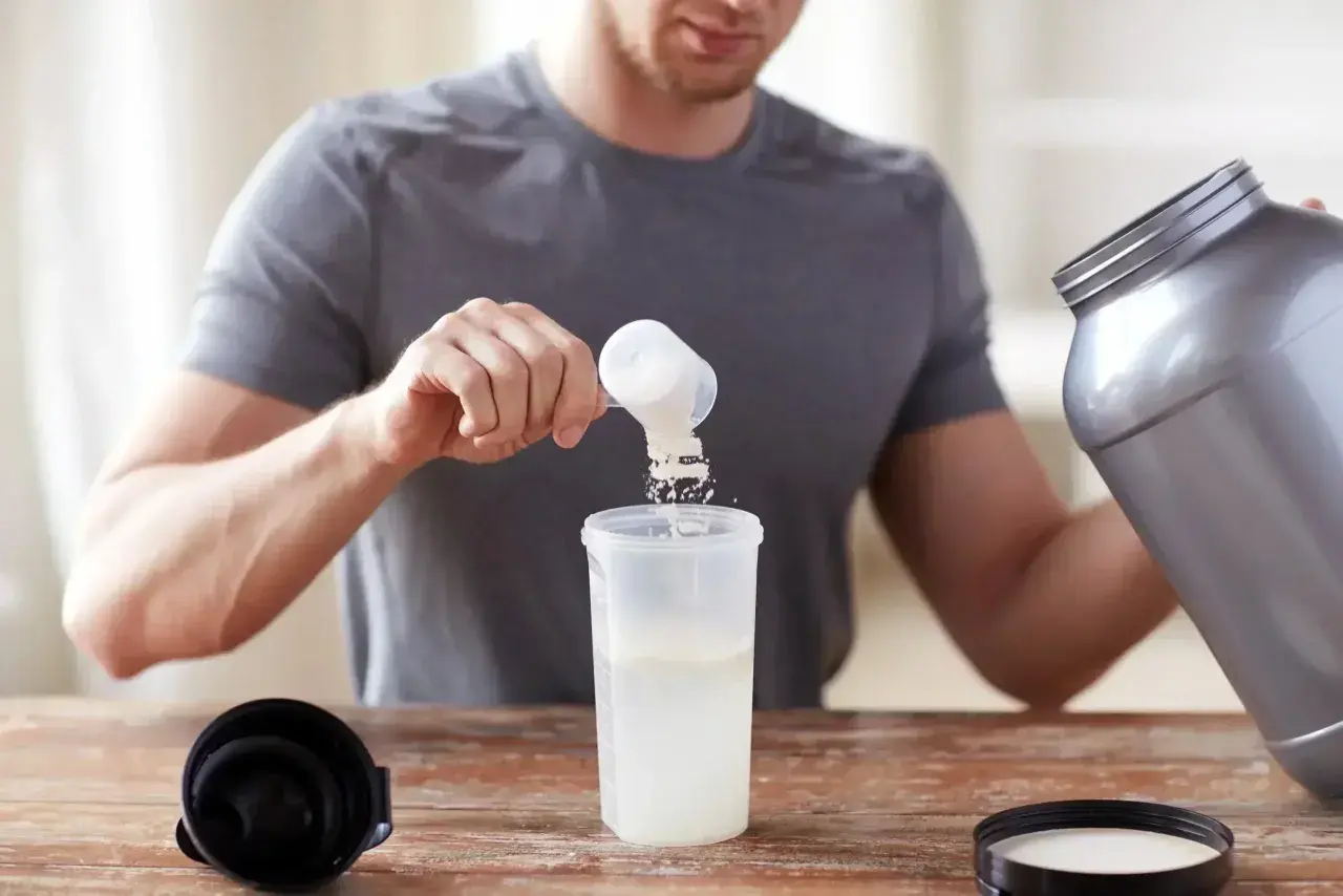 Hombre preparando su batido de proteina con agua o leche. Añade el polvo a un vaso mezclador.
