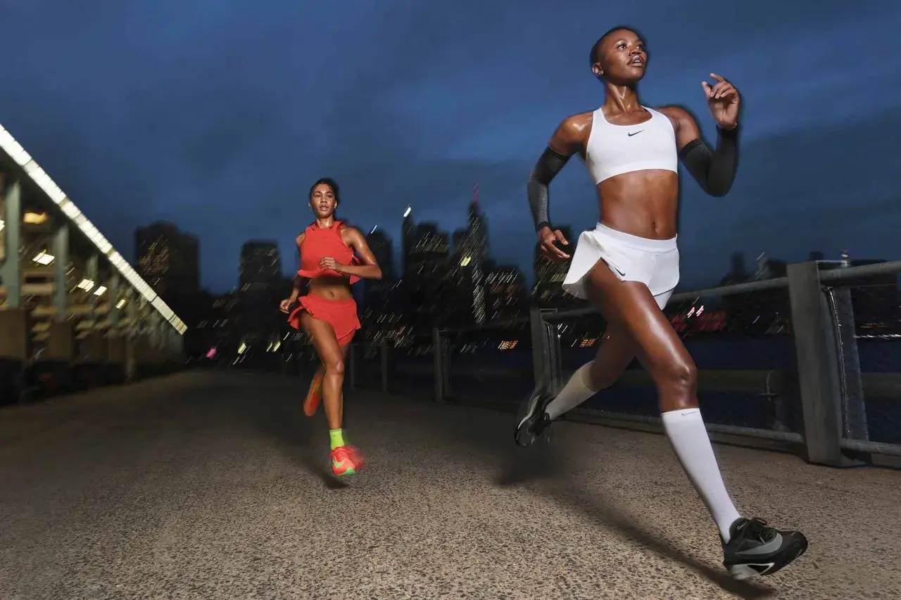 Dos corredoras entrenan al anochecer en la ciudad, aprendiendo como respirar al correr para mejorar su rendimiento.