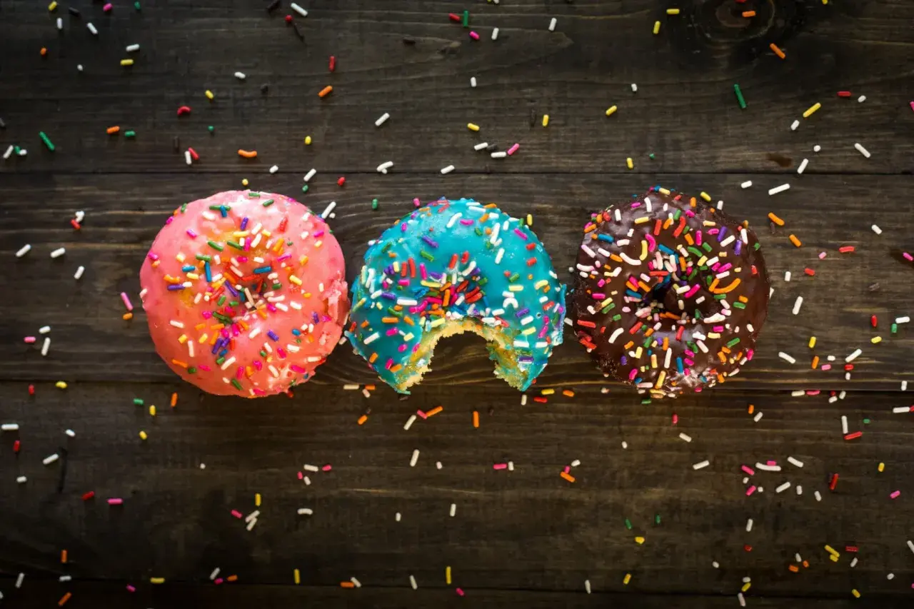 Tres donas coloridas con chispas, una mordida en la azul. ¡Un festín visual que desafía la dieta inversa!