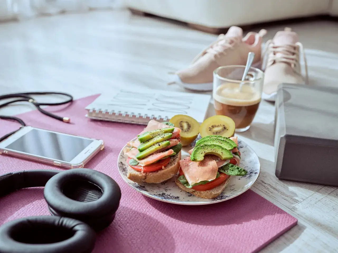 Dos sándwiches con aguacate y jamón serrano, ideales para que picar entre horas saludable. Junto a unas zapatillas deportivas y café.