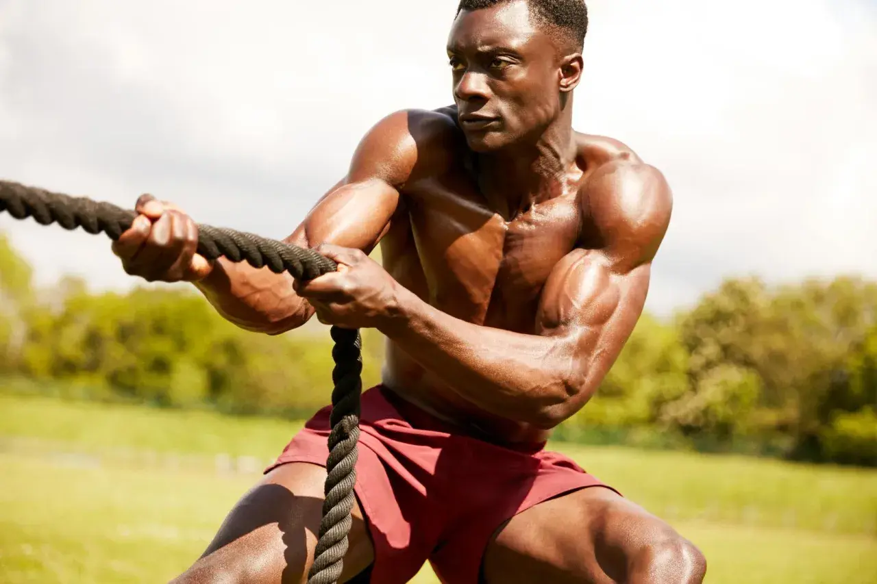 Hombre musculoso en entrenamiento espartano, tirando de una cuerda con fuerza.