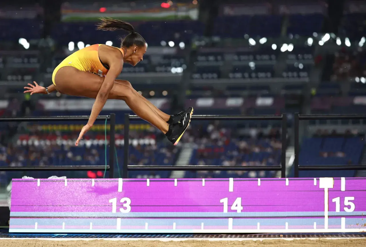 Ana Peleteiro en pleno salto de longitud, buscando su mejor marca. La atleta española vuela sobre la arena, superando los 14 metros.