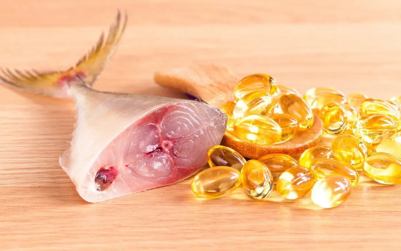 Un trozo de pescado fresco junto a cápsulas doradas, representando los **aceite de hígado de bacalao beneficios** para la salud.