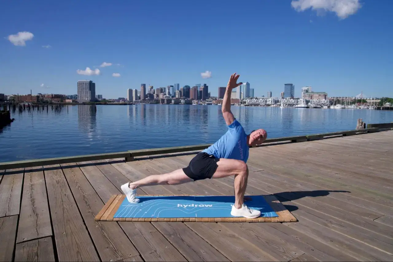 Hombre haciendo ejercicio en un muelle con Boston de fondo. Es bueno hacer ejercicio con agujetas para mejorar la flexibilidad.
