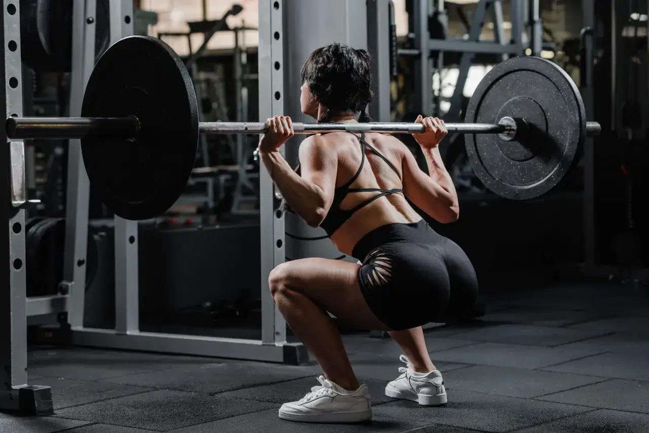 Mujer realizando sentadillas con barra, parte de su rutina de glúteos en el gym.