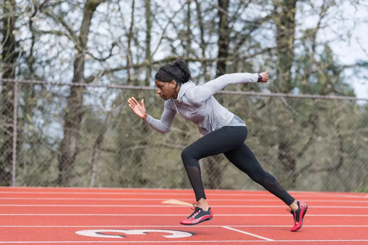 Atleta negra en plena carrera, con determinación en su rostro. La serie running la impulsa hacia adelante en la pista.