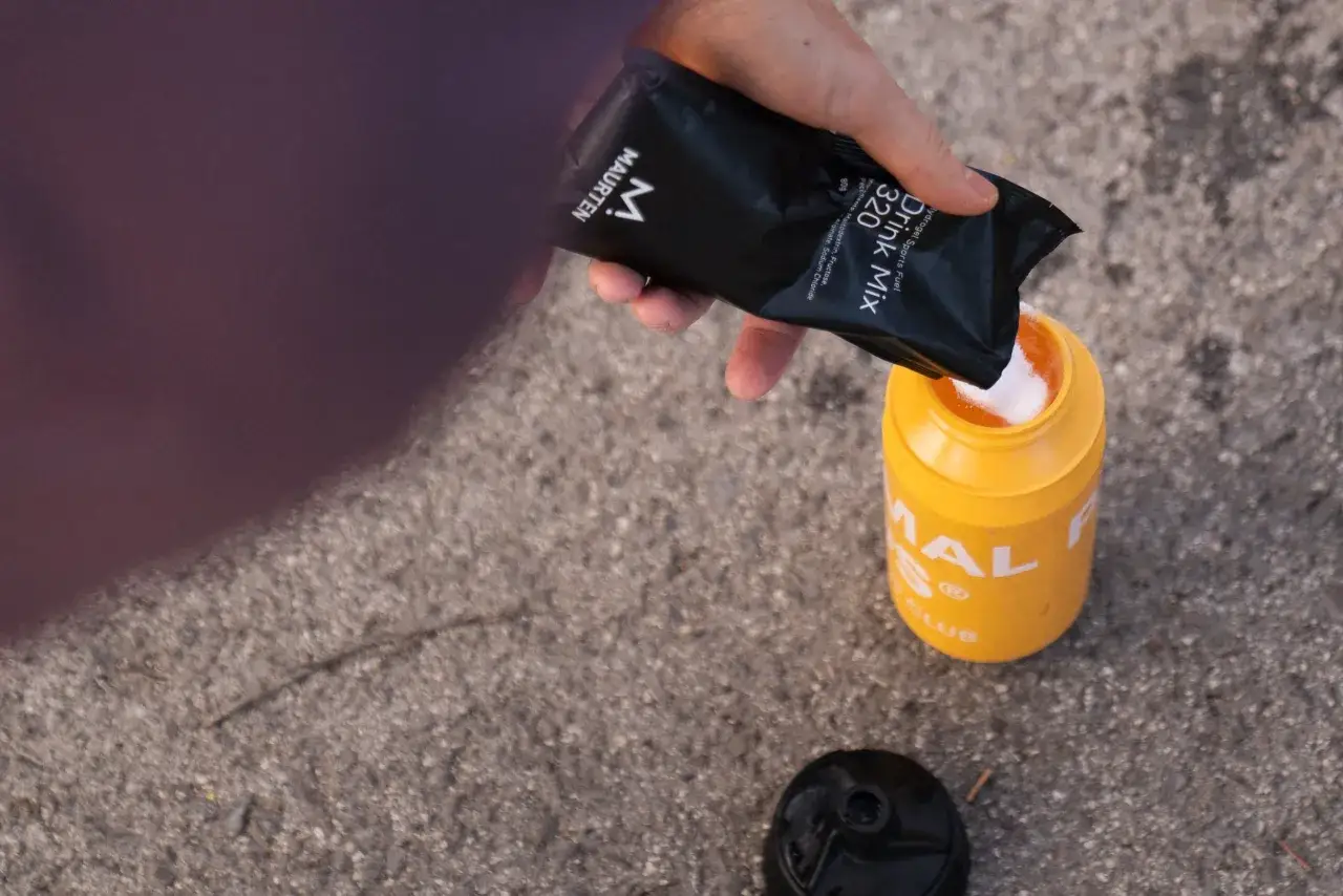 Persona vierte polvo de maltodextrina, que es mala, en un recipiente amarillo para bebida deportiva.