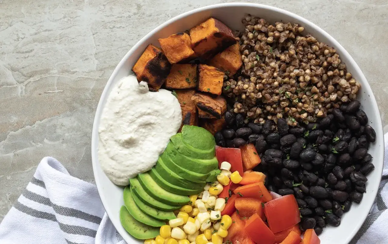 Un taz&oacute;n vibrante muestra qu&eacute; come un vegano: batata asada, aguacate, frijoles negros, ma&iacute;z, pimientos y una cremosa salsa blanca.