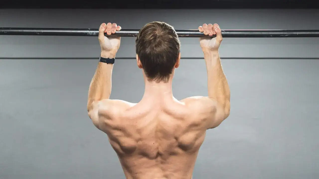 Hombre realizando dominadas supinas, mostrando su espalda musculosa y brazos fuertes.