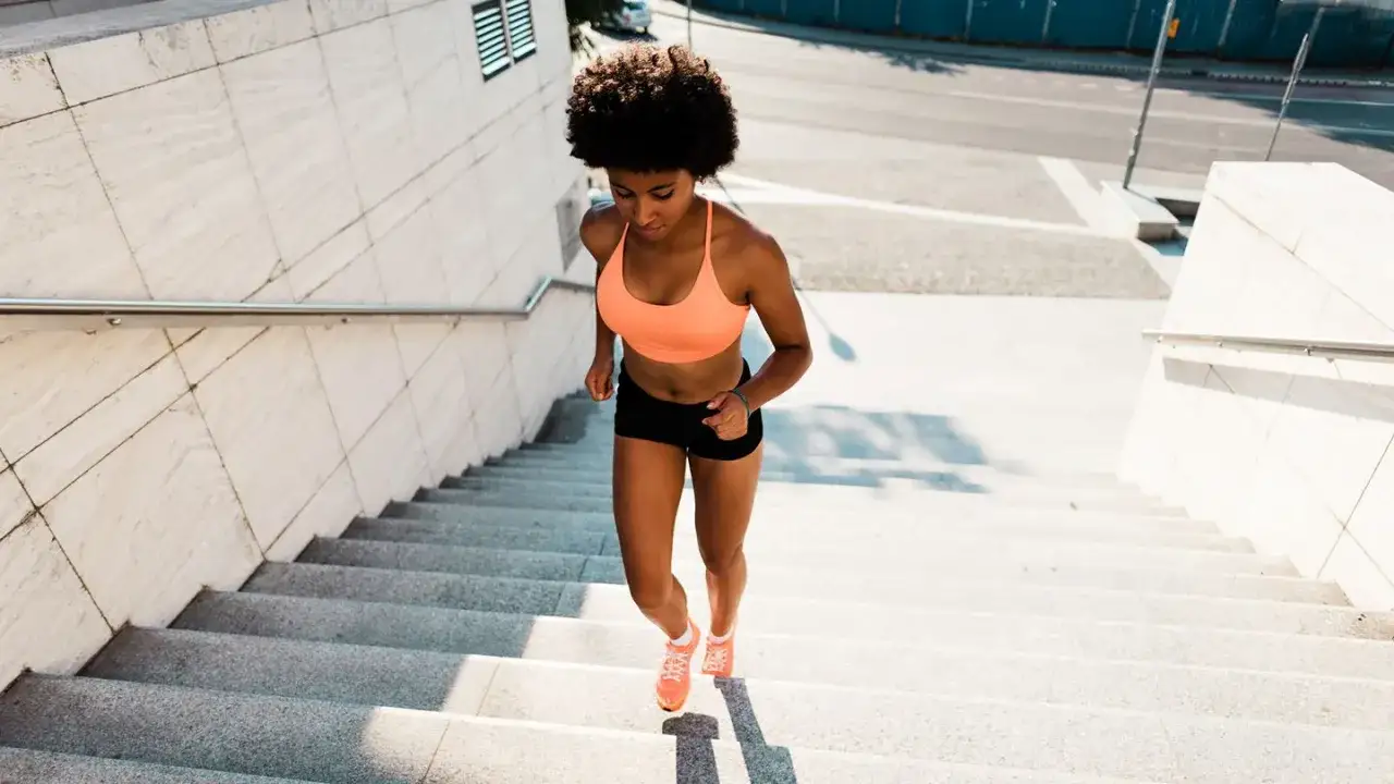 Mujer joven con afro subiendo escaleras, disfrutando de los subir escaleras beneficios para su entrenamiento.