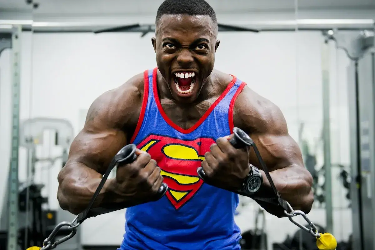 Hombre musculoso con camiseta de Superman entrenando en el gimnasio, mostrando la intensidad de cómo se toma la creatina para ganar fuerza.