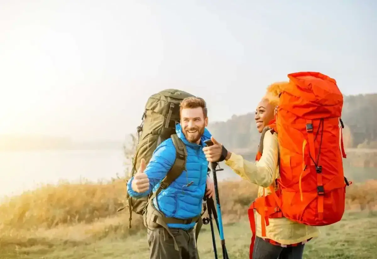 Pareja sonriente con mochilas enormes, disfrutando de su camino de Santiago corriendo.