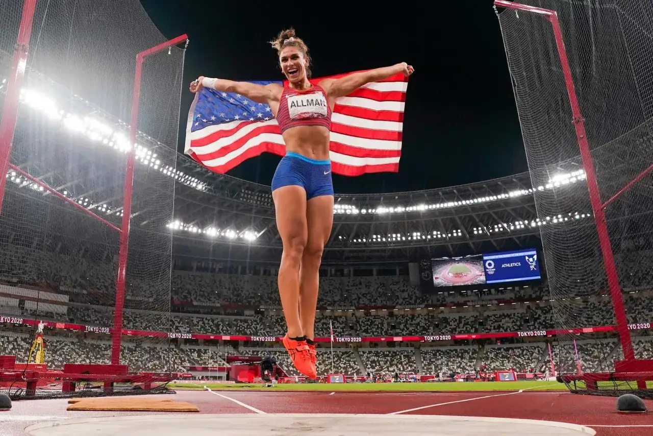 Valarie Allman salta en el aire con la bandera de EE. UU. tras ganar el oro en lanzamiento de disco en Tokio 2020.