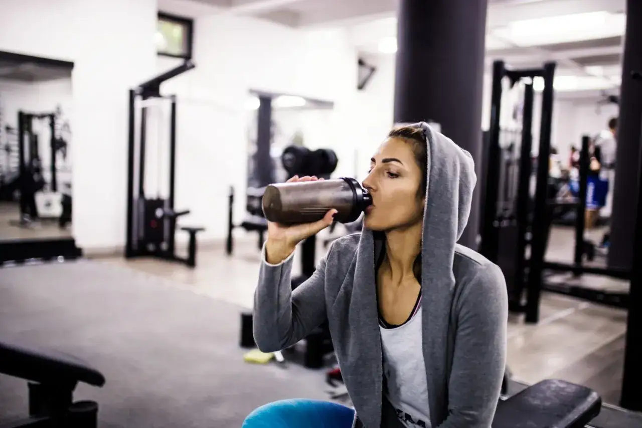 Mujer en gimnasio bebe batido. La caseína para que sirve: recuperación muscular y saciedad.