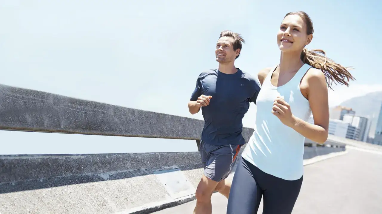 Pareja sonriente disfrutando de una carrera matutina, compartiendo consejos para correr mientras corren por un camino soleado.