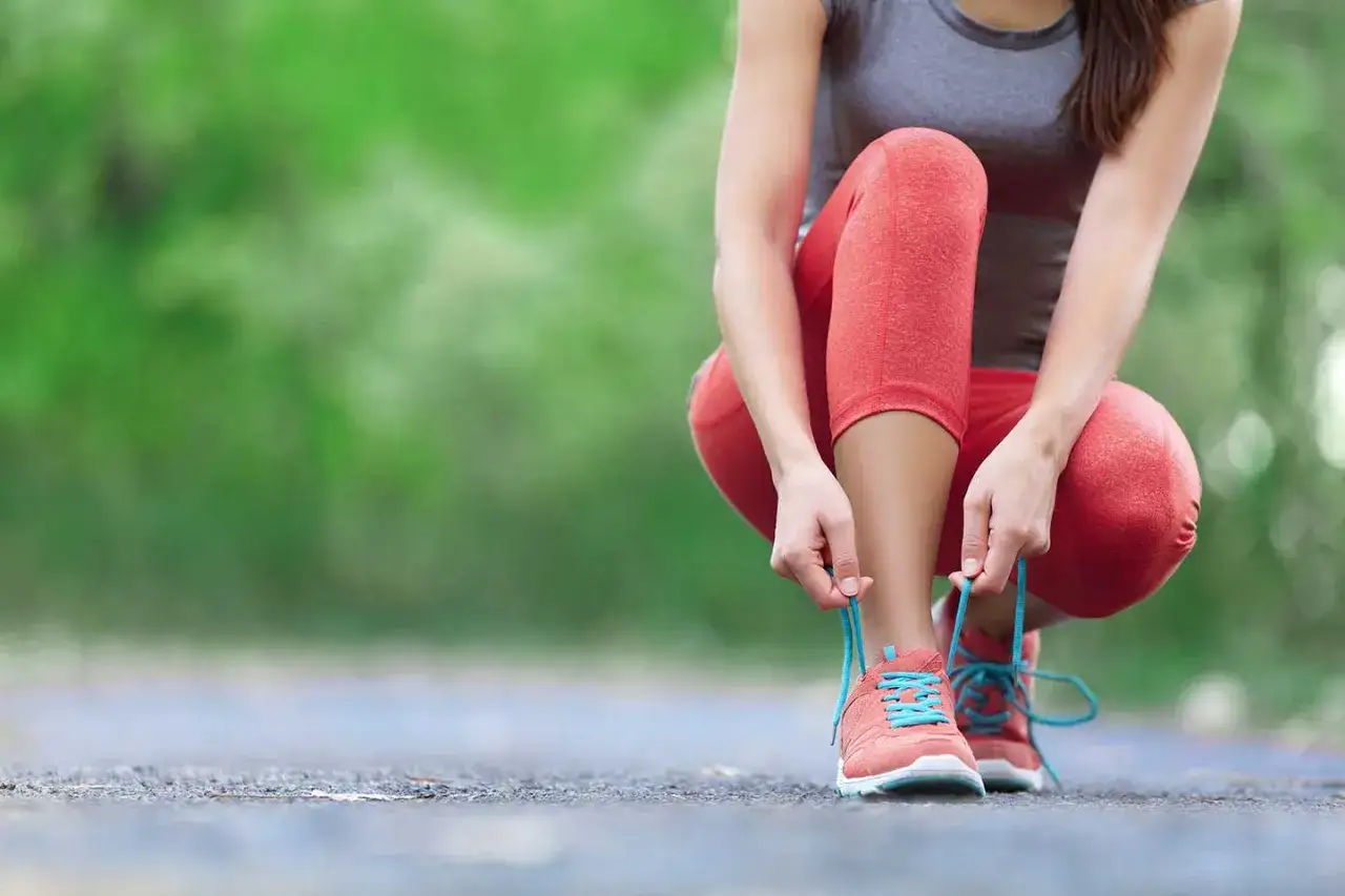 Mujer se agacha para atarse los cordones de sus zapatillas de running. Las noticias running te esperan.