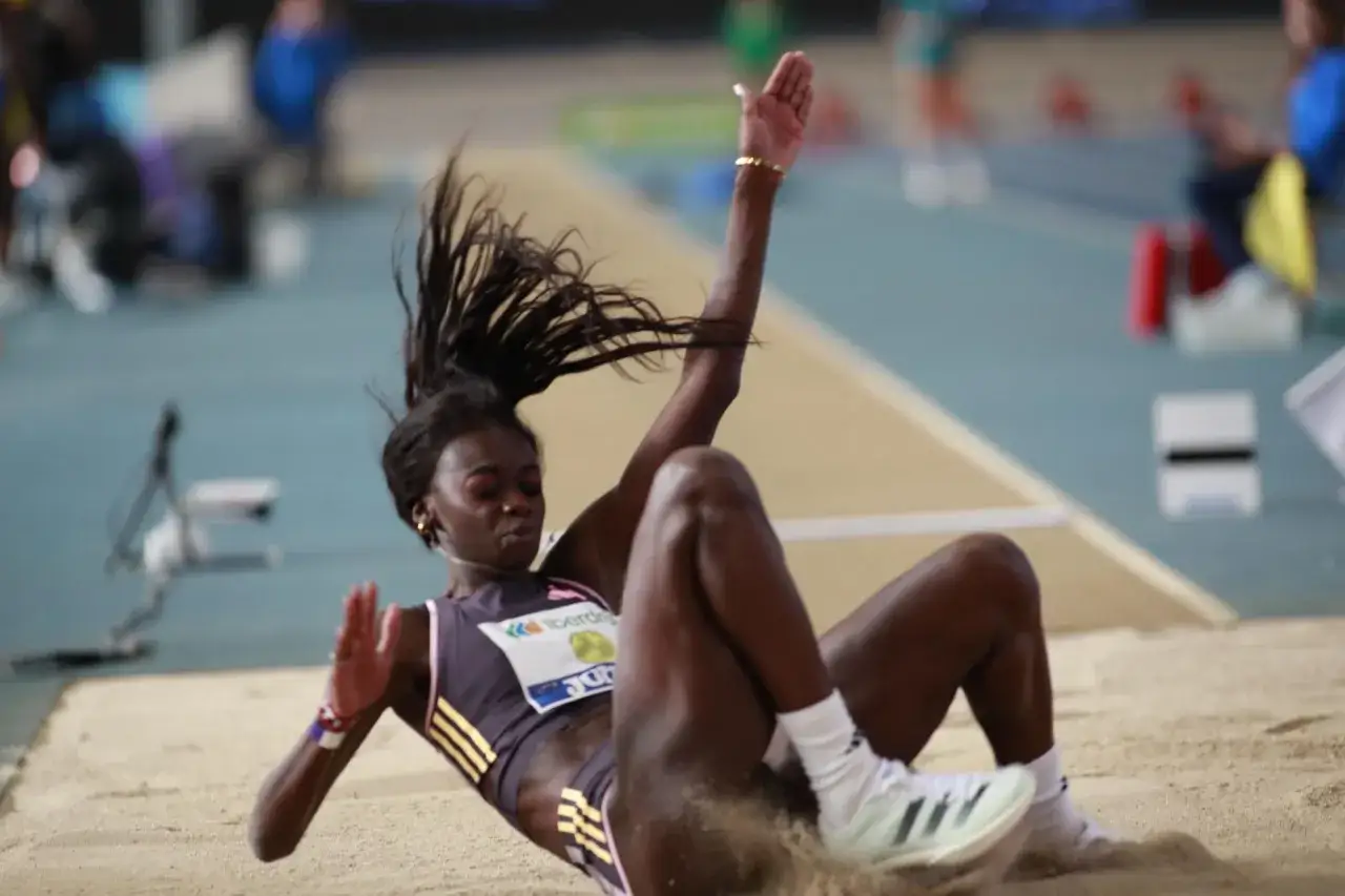 Atleta en pleno salto de longitud femenino, aterrizando en la arena con el cabello al viento.