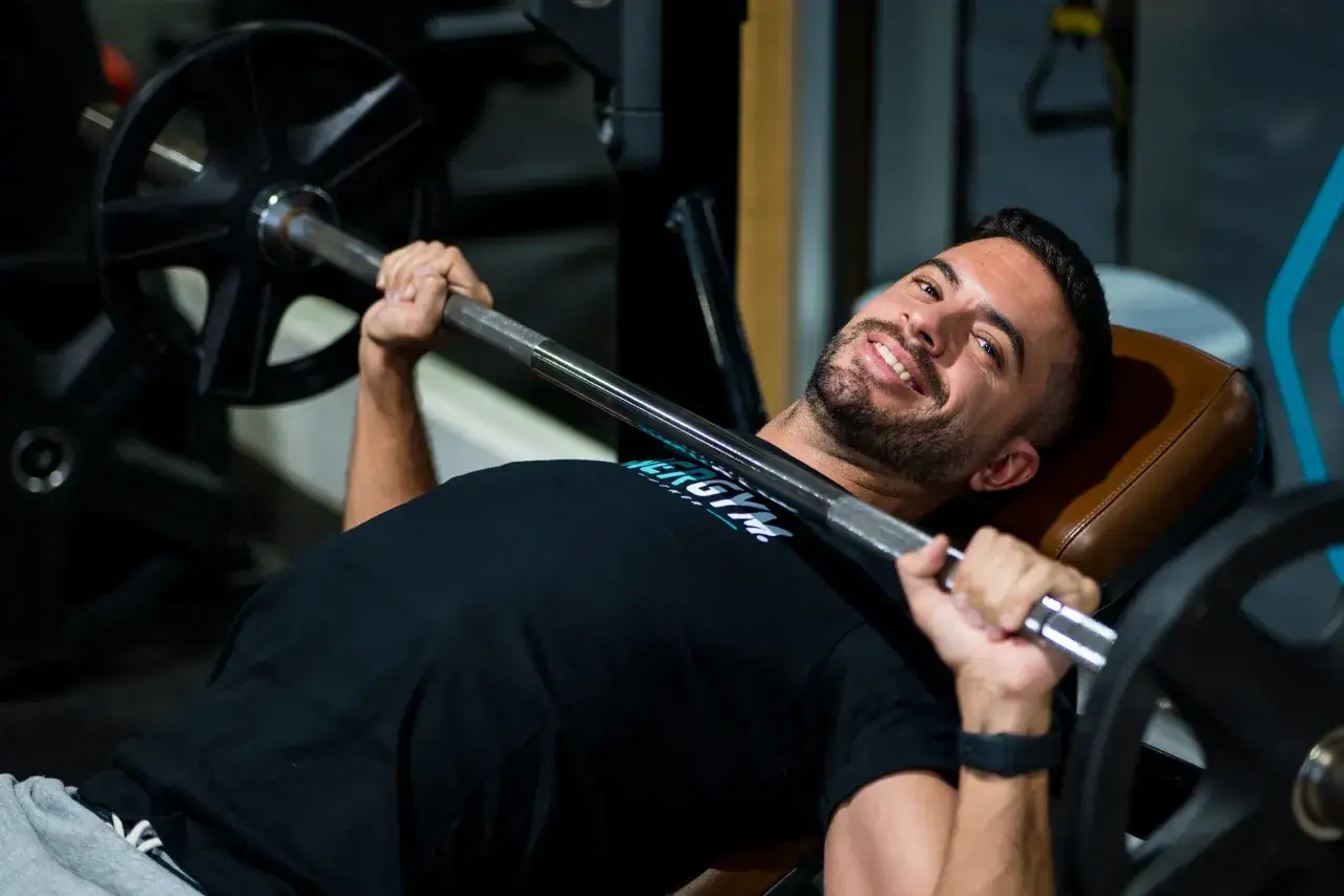 Hombre sonriente haciendo press de banca en el gimnasio.