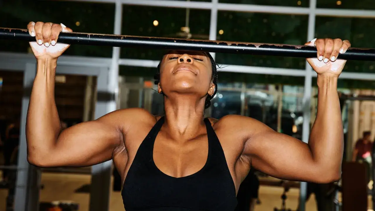 Mujer concentrada haciendo dominadas, demostrando los beneficios dominadas para la fuerza superior del cuerpo.