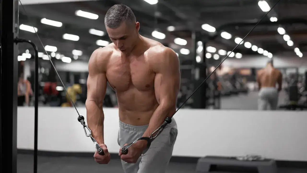 Hombre musculoso entrenando el pectoral superior en el gimnasio con poleas.