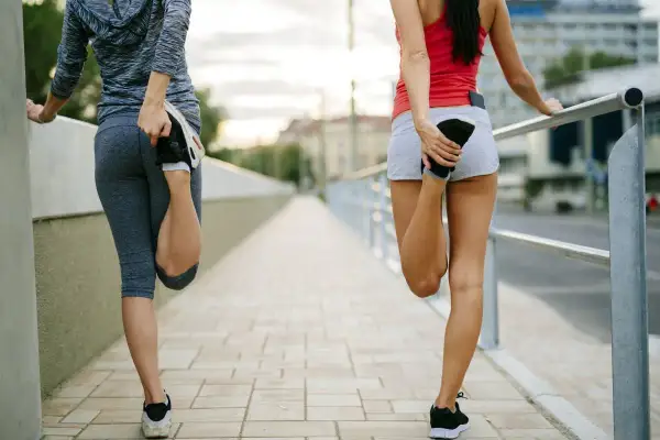 Dos mujeres estiran sus piernas en un puente. Saben que es bueno correr todos los días para mantenerse en forma.